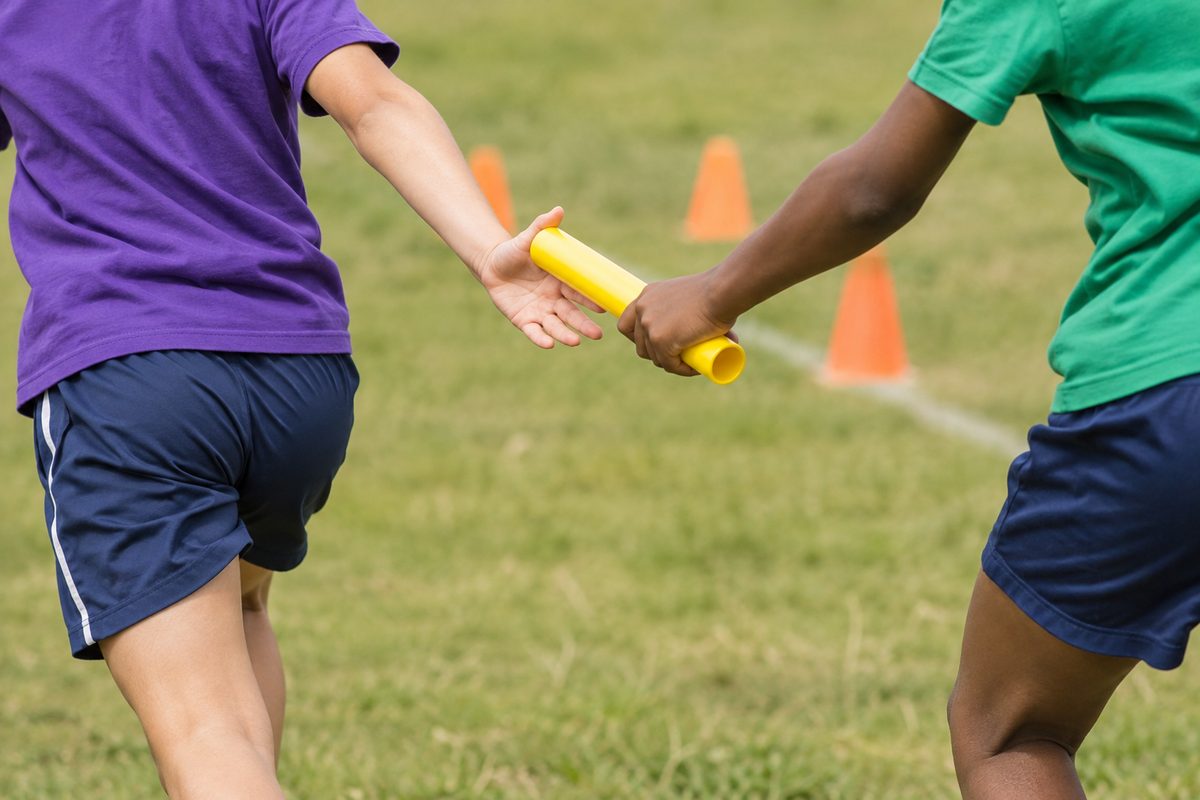 Two children passing a relay baton on a playing field